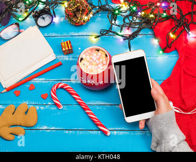 Smartphone con uno schermo nero in una donna la mano, accanto a un rosso tazza di caffè con marshmallow, vista dall'alto Foto Stock