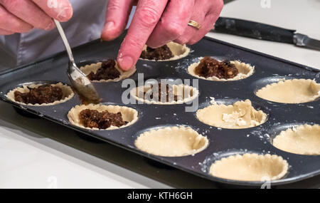 In prossimità delle mani dell'uomo con anello di nozze di riempimento torta tritare i casi con macinato e pronto per la cottura su una cucina bianca contatore per Natale Foto Stock