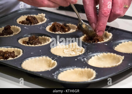 Primo piano delle mani dell'uomo che riempiono le casse di torta mince tritacambiare pronto per la cottura su un bancone da cucina bianco Foto Stock