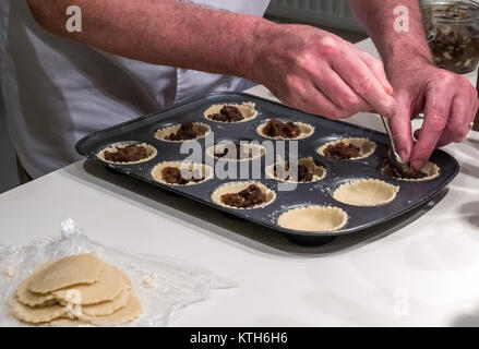 Chiusura del vecchio uomo in chef bianchi riempimento torta tritare i casi con macinato e pronto per la cottura a tempo di Natale su una cucina bianca counter Foto Stock