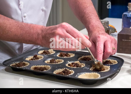 Chiusura del vecchio uomo in chef bianchi riempimento torta tritare i casi con macinato e pronto per la cottura a tempo di Natale su una cucina bianca counter Foto Stock