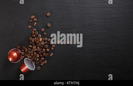 Rosso di caffè espresso e di capsule di caffè in grani su sfondo nero, vista dall'alto con spazio per il testo Foto Stock