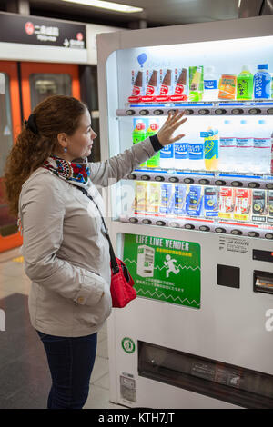 Giappone, Kyoto-CIRCA APR, 2013: Caucasian giovane donna è vicino il giapponese distributori automatici con bevande soda. Tenta di acquistare bevande. Distributore automatico tradizionale boxe Foto Stock