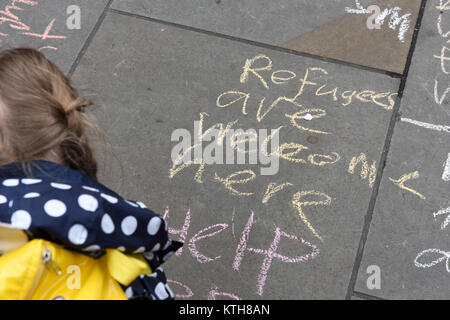 Un bambino protester sta scrivendo "I rifugiati sono benvenuti qui" e "Aiutare i bambini rifugiati" i messaggi sul marciapiede in sede ONU Anti-Racism giorno a Londra, Regno Unito. Foto Stock