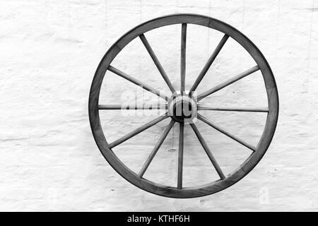 Vecchio carrello di legno ruota sospesa sulla parete rurale, in bianco e nero Foto Stock