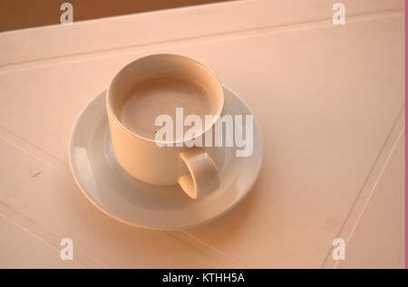 Un caldo il caffè amaro su un bianco tavolo di plastica con un cucchiaio e piattino sotto in attesa di qualcuno a bere in una zolla di terreno meteo nel dicembre 2017. Foto Stock