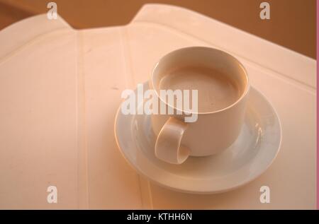 Un caldo il caffè amaro su un bianco tavolo di plastica con un cucchiaio e piattino sotto in attesa di qualcuno a bere in una zolla di terreno meteo nel dicembre 2017. Foto Stock