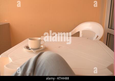 Un caldo il caffè amaro su un bianco tavolo di plastica con un cucchiaio e piattino sotto in attesa di qualcuno a bere in una zolla di terreno meteo nel dicembre 2017. Foto Stock