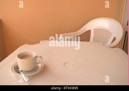 Un caldo il caffè amaro su un bianco tavolo di plastica con un cucchiaio e piattino sotto in attesa di qualcuno a bere in una zolla di terreno meteo nel dicembre 2017. Foto Stock