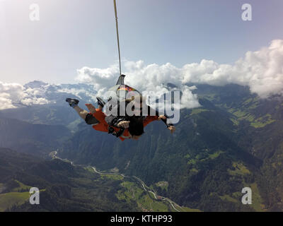 Questo lo skydiving in tandem e team sta godendo il volo panoramico su una bella montagna e lago di zona. Check out la faccina sorridente dal passeggero! Foto Stock