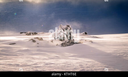 Una roccia coperte da neve fresca. Il sole è appena rottura attraverso e un forte vento soffiava ancora i fiocchi di neve attraverso l'aria. Foto Stock