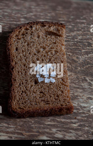 Pezzo ruvido pane di segale con sale grosso su uno sfondo di legno, macro shot Foto Stock