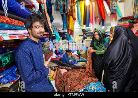 Yazd, Iran - 22 Aprile 2017: una giovane iraniana commerciante tessile nel bazaar, attesa per le donne musulmane di scegliere la merce per l'acquisto. Foto Stock