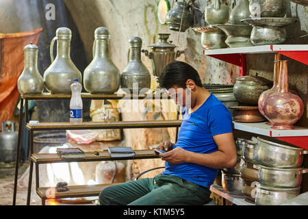 Yazd, Iran - 22 Aprile 2017: un giovane uomo utilizza uno smartphone mentre è seduto su una sedia in un negozio di stagno. Foto Stock