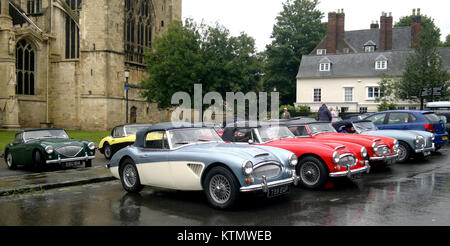 Un gruppo di auto Austin Healey è parcheggiato fuori dalla Cattedrale di Gloucester in questa fotografia. L'evento riunisce gli appassionati della classica auto sportiva britannica, mostrando i veicoli di fronte alla storica cattedrale. L'incontro mette in evidenza il legame tra la cultura automobilistica d'epoca e i monumenti storici. Foto Stock