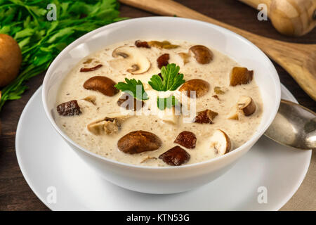 Un primo piano di una piastra di un fungo minestra in crema con champignon, cremini, prezzemolo fresco e pepe, al buio su un sfondo rustico Foto Stock