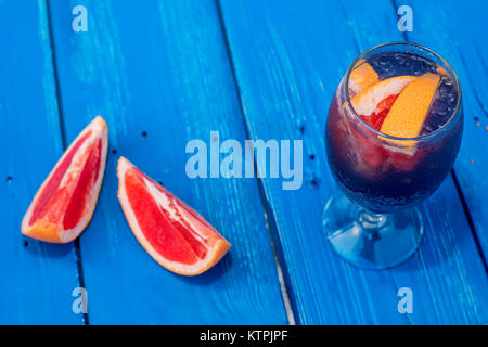 Chiudere il vetro con cocktail scuro e pompelmo su blu sullo sfondo di legno Foto Stock