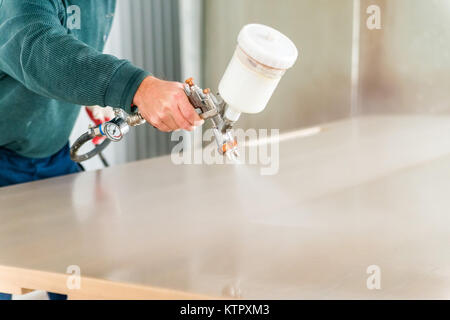 Close up lavoratore la mano con la pistola a spruzzo Applicazione di vernice su di legname, la colorazione Foto Stock