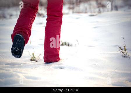 Passeggiate nel gelido inverno sulla neve in pantaloni rossi e scarponi da neve Foto Stock