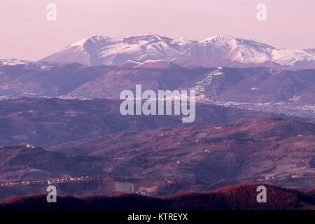 Umbria Valle d'inverno, con una vista della città di Gubbio con il grande albero di Natale illuminato sul lato della montagna e del Monte Cucco coperte da neve Foto Stock