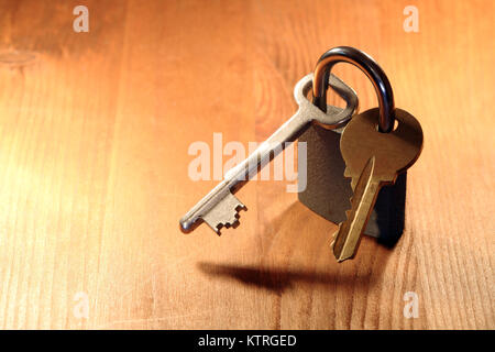 Piccolo lucchetto chiuso con due chiavi diverse in piedi su sfondo di legno Foto Stock