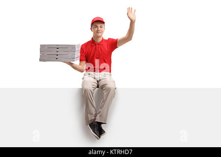 Teenage consegna pizza ragazzo con una pila di scatole per pizza seduti su un pannello e agitando isolati su sfondo bianco Foto Stock