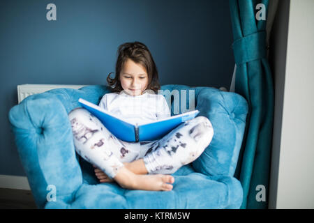 Funny happy toddler girl leggendo un libro e giocare a letto. Bambini giocano in casa. Vivaio bianco. Bambino in camera da letto di sole. Bambini leggere e studiare. Interio Foto Stock