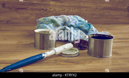 Bianco e nero barattoli di vernice con pennello e straccio sporchi su sfondo di legno Foto Stock
