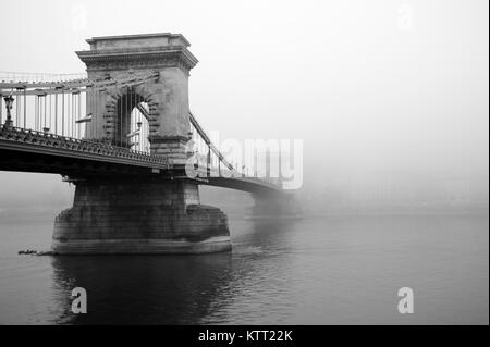 Fotografia in bianco e nero di nebbia rotolamento sotto il Ponte della Catena lungo il Danubio, Budapest, Ungheria Foto Stock