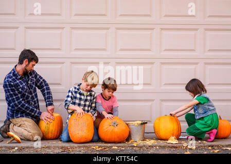 Tre figli e il loro padre carving zucche di Halloween Foto Stock