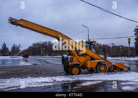 Macchina pale da neve sulla strada e il caricamento di neve in un carrello . Macchine arancione, neve pulitori , vicino al semaforo . Mosca , Russia . Foto Stock