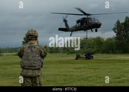 Un U.S. Soldato dell'esercito assegnato al Bravo batteria 2° Battaglione, xv campo reggimento di artiglieria, 2° Brigata Team di combattimento, scatta una foto di un UH-60 Black Hawk elicottero sollevamento di un M119A2 Obice sul tamburo di Fort, N.Y., luglio 14, 2017. Soldati dal Bravo batteria sono stati condurre aria incursioni di artiglieria. (U.S. Esercito nazionale Guard foto di PFC. Andrew Valenza) Foto Stock