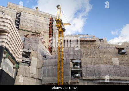 Giallo gru a torre lavora vicino a casa di cemento con i ponteggi, edificio è in fase di costruzione Foto Stock