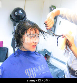 Giovane donna avente un taglio di capelli in seduta parrucchiere. Ella ha un naturale scuro capelli arricciati. La stilista donna utilizza le forbici per tagliare lungo le ciocche di capelli. Foto Stock