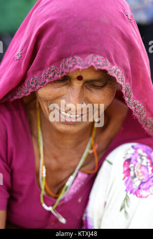Ritratto di donna indiana in un rosa vestiti tradizionali con la testa coperta con velo di colore rosa, guardando verso il basso, villaggio nei pressi di Pushkar, Rajasthan, India. Foto Stock
