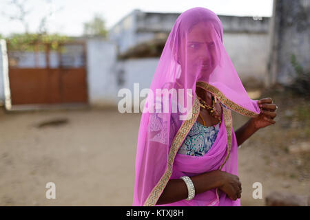Ritratto di giovane donna indiana indossando sari e una rosa velo che copre il volto nel suo cortile, villaggio nei pressi di Pushkar, Rajasthan, India. Foto Stock
