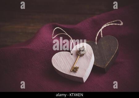 Vintage Valentine cuori di legno con una chiave magica sul rosso scuro igienico ith uno sfondo marrone Foto Stock