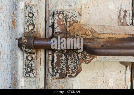 Molto vecchio, deteriorando gate chiavistello a scatto in una posizione bloccata, completa di parti di ricambio si arrugginiscano e peeling vernice bianca sulla porta di legno. Strettamente ritagliato un Foto Stock