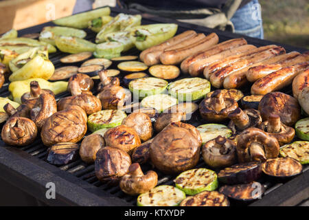Un assortimento di deliziosi piatti di carne alla brace con verdure sopra il barbecue sul carbone. Salsicce, bistecche, pepe, funghi e zucchine. Foto Stock
