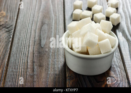 Zucchero bianco in vaso su sfondo di legno. Messa a fuoco selettiva, orizzontale. Alcuni cubetti di zucchero sono vicino al bicchiere pieno con zucchero bianco. Aspirazione di bad calor Foto Stock