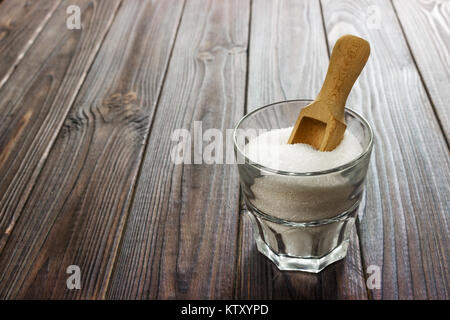 Lo zucchero bianco cristallizzato nella tazza bianca con il cucchiaio di legno su sfondo di legno. Foto Stock