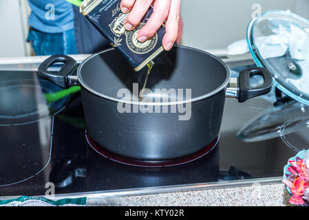 Primo piano versando vegetali Olio di oliva in padella caserole. Foto Stock