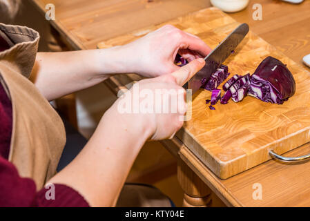 Mani femminili trinciatura di cavolo rosso con il coltello sulla tavola di legno. Foto Stock