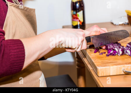 Mani femminili trinciatura di cavolo rosso con il coltello sulla tavola di legno. Foto Stock