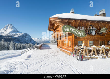 Alpine chalet di legno sul Ehrwalder Alm ski resort circondato da un soleggiato paesaggio innevato , Tirolo, Austria Foto Stock