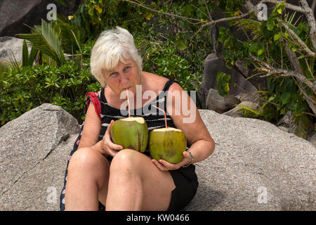 Donna di bere con una cannuccia dal succo di cocco, latte di cocco sulla spiaggia di Anse Source d'Argent, La Digue, Seicelle Foto Stock