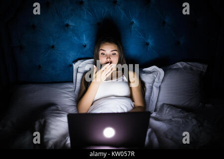 Giovani belle ispanico internet addict donna in pigiama sul letto di casa camera da letto lavorando annoiato e stanco con computer portatile a tarda notte Foto Stock