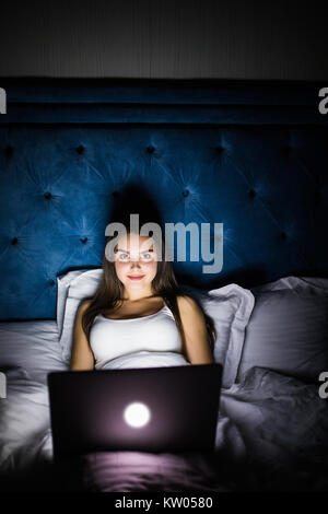 Giovani belle ispanico internet addict donna in pigiama sul letto di casa camera da letto lavorando annoiato e stanco con computer portatile a tarda notte nel buio ro Foto Stock