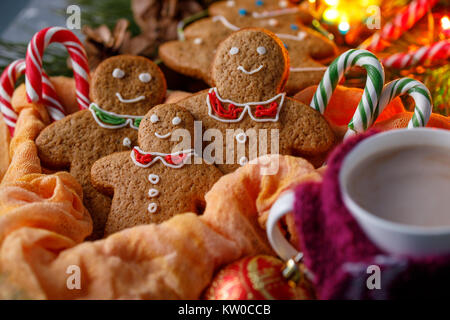 Atmosfera natalizia di magia. Funny sorridente piccoli uomini e canne di caramella. Gingerbread e cioccolata calda in una tazza con un allegro sciarpa. Foto Stock