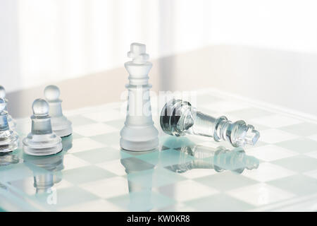 Un chiaro e un vetro smerigliato gioco di scacchi appena finito. Quella che il re si eleva alto mentre gli altri stabilisce nella sconfitta. Lo sfondo è bianco. Foto Stock